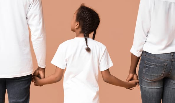 Family connection. Rear view of african mother, father and daughter holding hands together, yellow studio background, closeup