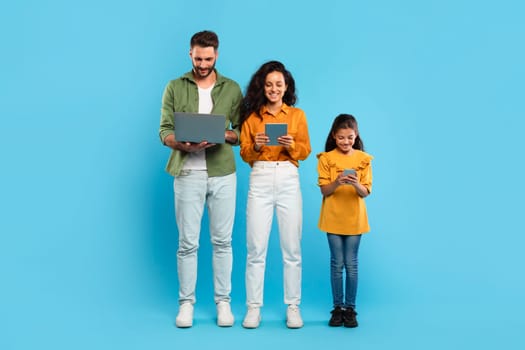 A man, woman, and young girl stand in a row against a light blue background. Family using various devices. Gadgets addiction