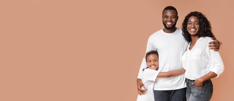 Beautiful African American family with daughter embracing and posing to camera over yellow studio background with copy space