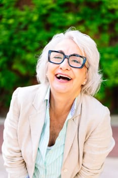 portrait of a middle age woman laughing happy looking at camera with blurred green plants background, concept of mature people lifestyle