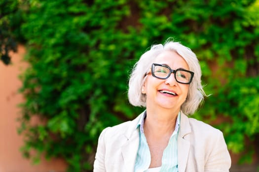 portrait of a middle age woman laughing happy with blurred green plants background, concept of mature people lifestyle, copyspace for text