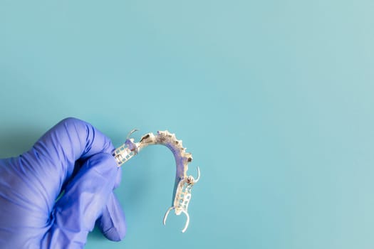Mockup Metal Frame Lower Partial Denture, Cobalt Chrome Dental Plate, Bridge Printed By 3d Printer in Doctor's Hand. Blue Background. Flat Lay Mockup. Copy Space For Text. Dentistry. Horizontal Plane