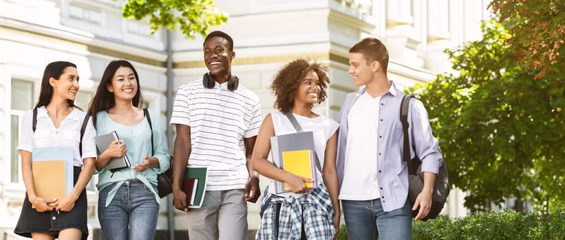 Happy university students walking together on campus, chatting and laughing outdoors during break, copy space