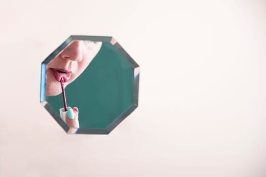 reflection of a woman in the mirror who paints her lips with lipstick, mirror hanging in zero gravity on peach fuzz background,