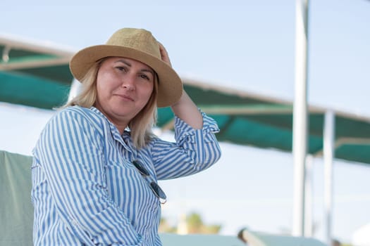 Young woman sitting on a sun lounger on the beach wearing a hat, looking tense, unable to relax even on vacation, deep in thought, midlife crisis