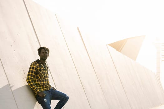 young african man leaning on a modern concrete structure at sunset, lifestyle concept