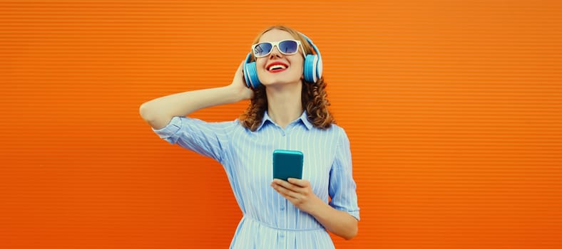 Happy smiling young woman listening to music in headphones with smartphone on orange background