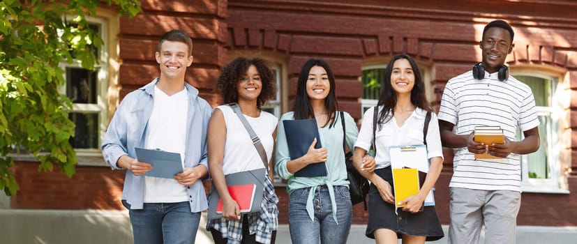 Happy multicultural students walking near university campus together, soending time outdoors after classes, free space