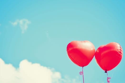 Red heart balloons floating in the blue sky with clouds, symbolizing love and romantic moments