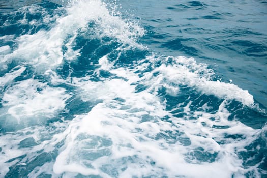 Wave on blue water and white foam on the tops of the waves from under the side of a floating boat, space for text