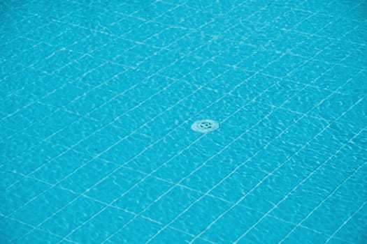 Defocused blurred transparent blue clear calm swimming pool water surface texture and water drain hole on the bottom, abstract background, place for text,
