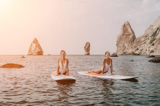 Woman sup yoga. Middle age sporty woman practising yoga pilates on paddle sup surfboard. Female stretching doing workout on sea water. Modern individual hipster outdoor summer sport activity