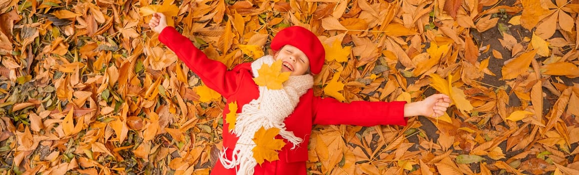 An overhead view of a caucasian girl in a red coat and beret lies on yellow foliage. Walk in the park in autumn. Widescreen