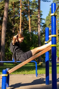 A teenage girl doing abdominal crunches. A girl performs exercises for the development of core muscles on a training ground in a city park