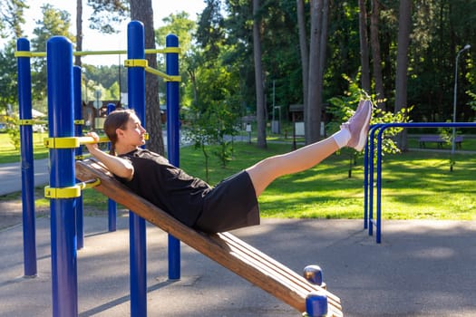 A teenage girl doing abdominal crunches. A girl performs exercises for the development of core muscles on a training ground in a city park