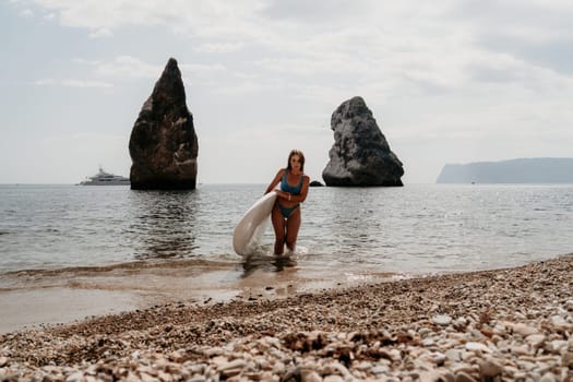 Close up shot of beautiful young caucasian woman with black hair and freckles looking at camera and smiling. Cute woman portrait in a pink bikini posing on a volcanic rock high above the sea