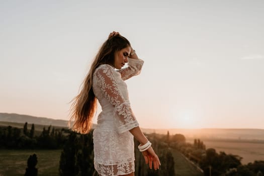 Romantic beautiful bride in white dress posing with sea and mountains in background. Stylish bride standing back on beautiful landscape of sea and mountains on sunset