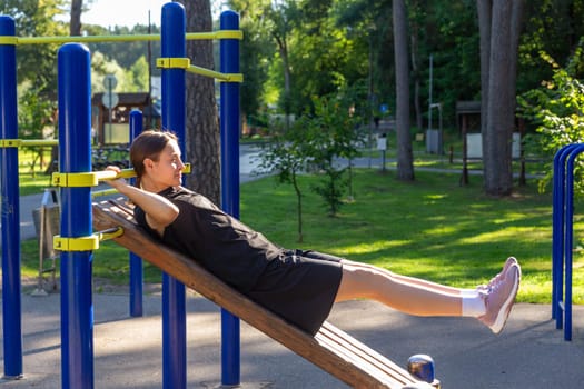 A teenage girl doing abdominal crunches. A girl performs exercises for the development of core muscles on a training ground in a city park