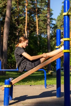 A teenage girl doing abdominal crunches. A girl performs exercises for the development of core muscles on a training ground in a city park