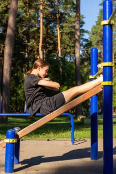 A teenage girl doing abdominal crunches. A girl performs exercises for the development of core muscles on a training ground in a city park