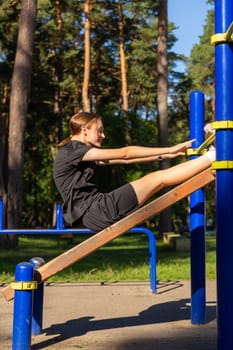 A teenage girl doing abdominal crunches. A girl performs exercises for the development of core muscles on a training ground in a city park