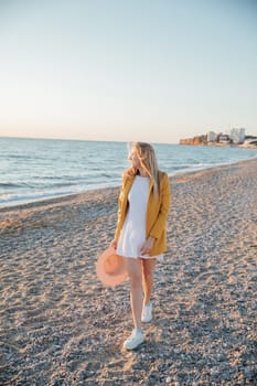 woman walks along the seashore with a hat in her hands