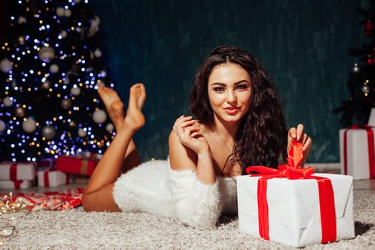 a beautiful brunette woman lying at the Christmas tree with gifts