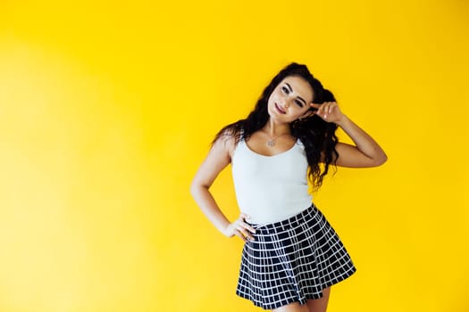 a woman in a plaid short skirt and a white T-shirt poses on a yellow background