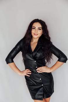 woman in a black leather dress posing on a white wall in a room