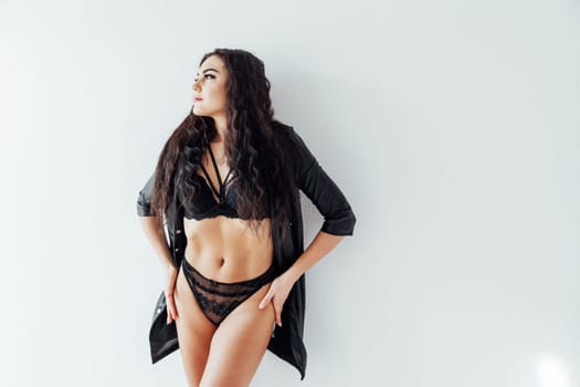 brunette woman in black underwear stands against a white wall