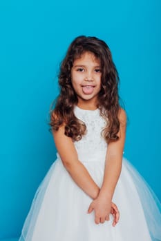 little girl in a white dress shows her tongue on a blue background