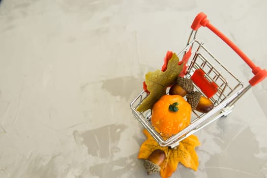 Grocery cart with decorative pumpkins and maple leaves on a concrete background. The concept of the autumn sales. Black Friday and cyber Monday. Space for text.