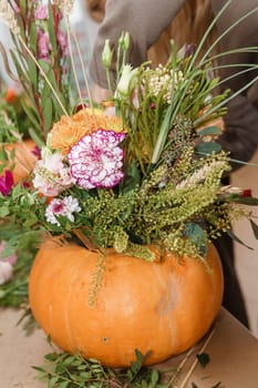 Flower arrangement in a pumpkin, autumn interior decor. Creating handmade autumn decor