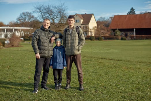 Family Harmony: Father, 40 Years Old, and Two Sons - Beautiful 8-Year-Old Boy and 17-Year-Old Young Man, Standing on the Lawn in a Park with Vintage Half-Timbered Buildings, Bietigheim-Bissingen, Germany, Autumn. Embrace the essence of family togetherness with this heartwarming image featuring a father, 40 years old, and his two sons - a beautiful 8-year-old boy and a 17-year-old young man. Standing on the lush lawn in a park with vintage half-timbered buildings in Bietigheim-Bissingen, Germany, this captures the warmth of familial bonds amidst the autumnal beauty.