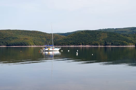 small yacht with lowered sail on a calm forest lake.