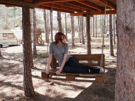 teenage girl on a swing made of wooden pallets in a pine forest.