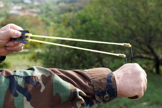 a stretched slingshot in male hands against a forest background.