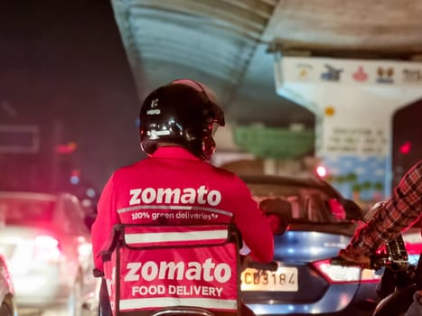 Delhi, India - 20th May 2023: Delivery boy rider from food delivery app Zomato stuck in traffic on a rainy night showing the busy lifestyle