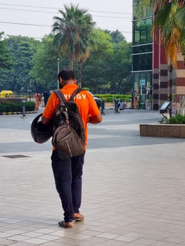 Delhi, India - 28th Oct 2023: Delivery boy rider from the food delivery app swiggy walking with a backpack searching for address