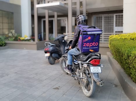 Delhi, India - 18th Dec 2022: Rider delivery boy from hyperlocal quick fast delivery app zepto standing outside a residential building showing the rapid rise of this startup