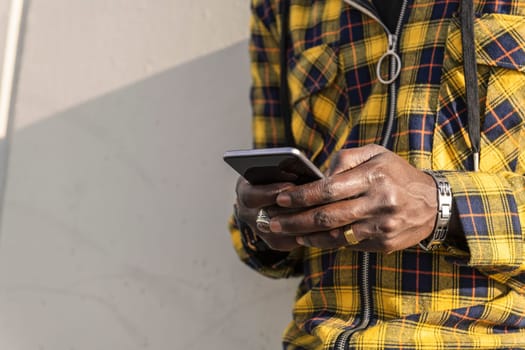 hands of an unrecognizable young african man writing a message on his phone leaning on a modern concrete structure, concept of lifestyle and technology
