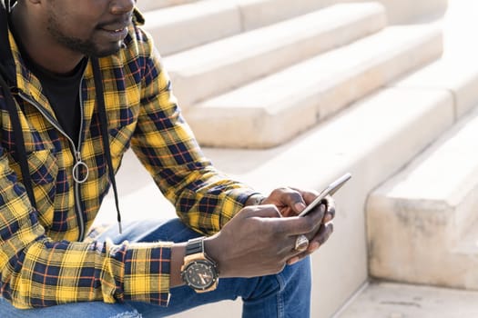unrecognizable young black man sitting on a concrete staircase with his phone, lifestyle and technology concept, copy space for text