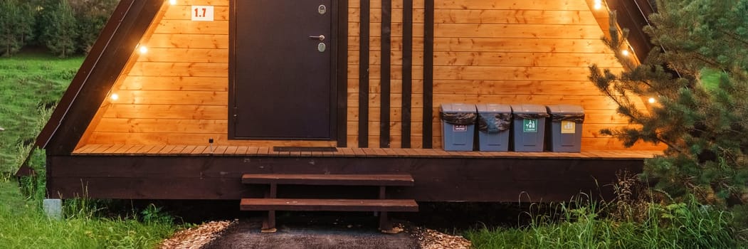 The concept of glamping and renting a chalet for weekend. Wooden house with a veranda in nature around coniferous trees.