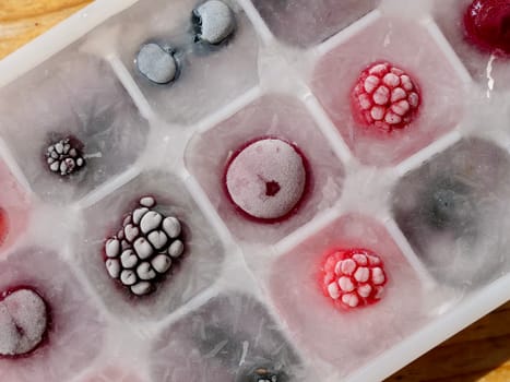 Frozen ice with berries in a container by the piece for making refreshing drinks or preserving vitamins and minerals seasonal cherries, raspberries, strawberries, blackberries, mulberries, blueberries
