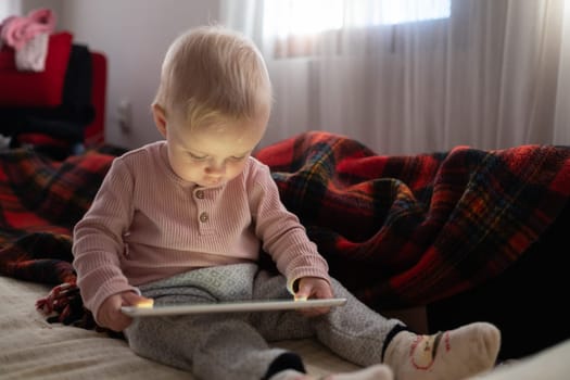 Toddler girl playing with digital wireless tablet computer on couch at home. Child and electronic devices concept.