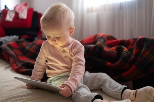 Toddler girl playing with digital wireless tablet computer on couch at home. Child and electronic devices concept.