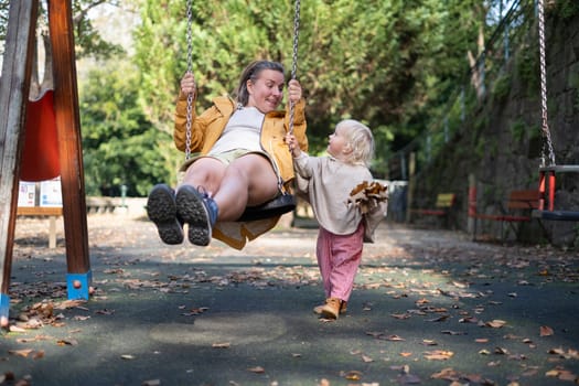 Smiling mother and daughter having good time on the playground swinging