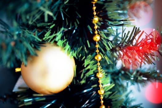 Yellow ball Christmas tree toy close up. Christmas ornament with lighted tree in background.