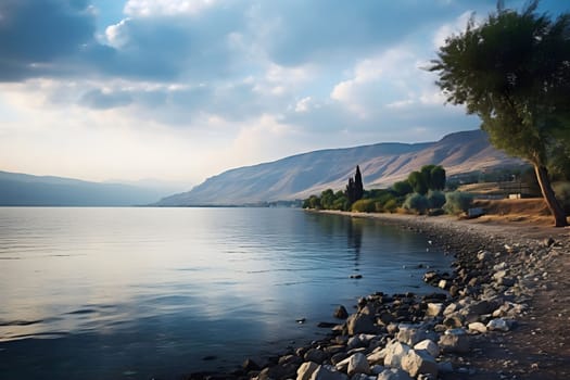 A tranquil lake with mountains in the background, reflecting the blue sky with white clouds. The shore is lined with trees and rocks, creating a serene and peaceful atmosphere.