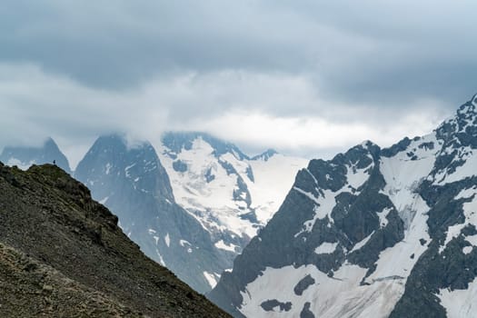 A drone flies over a mountain valley in the Caucasus Mountains. The valley is filled with green trees and a winding river. In the distance, a snow-capped peak rises above the valley.
